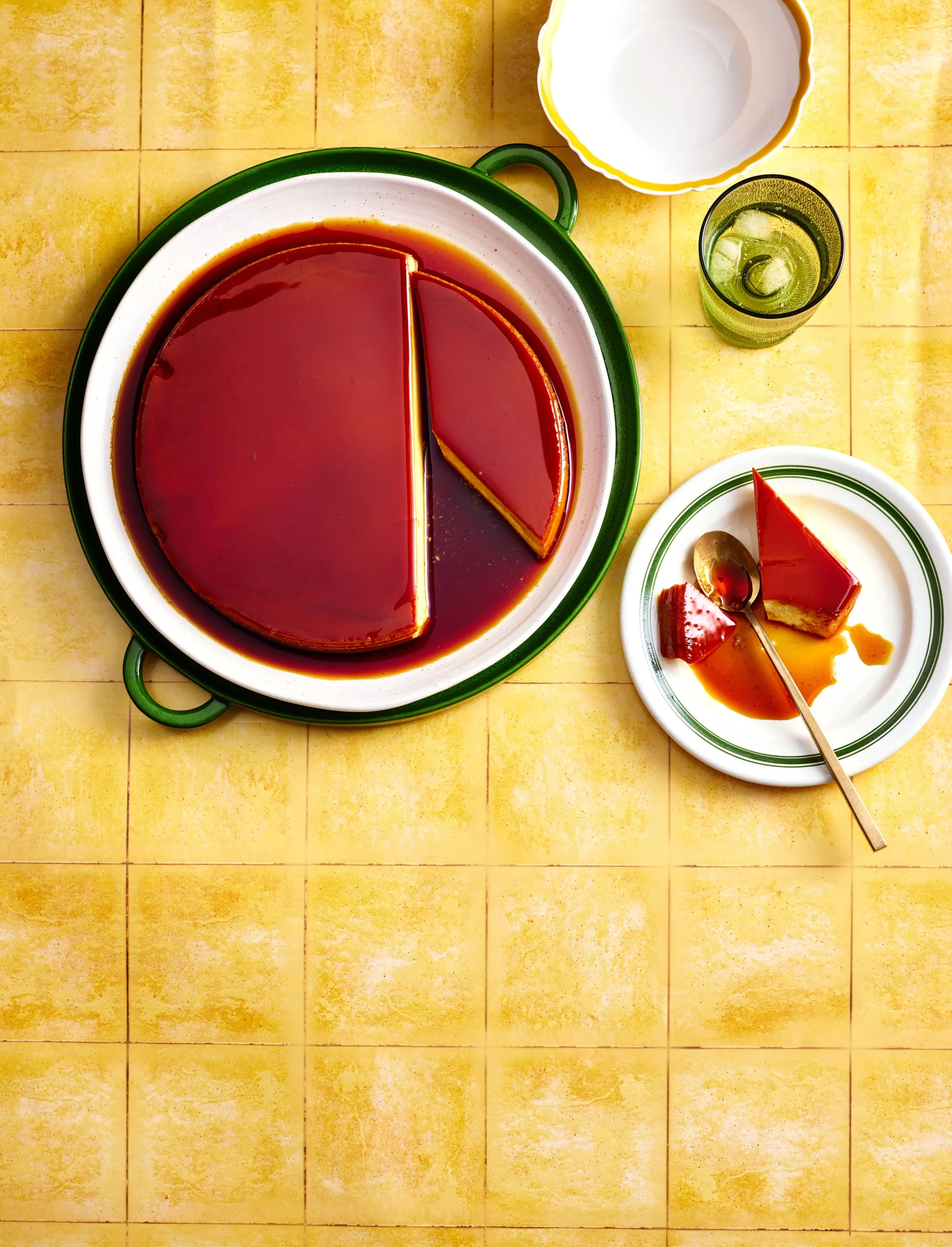 colin fassnidge's creme caramel cheesecake with slice cut out on separate plate sitting on bright tile like background