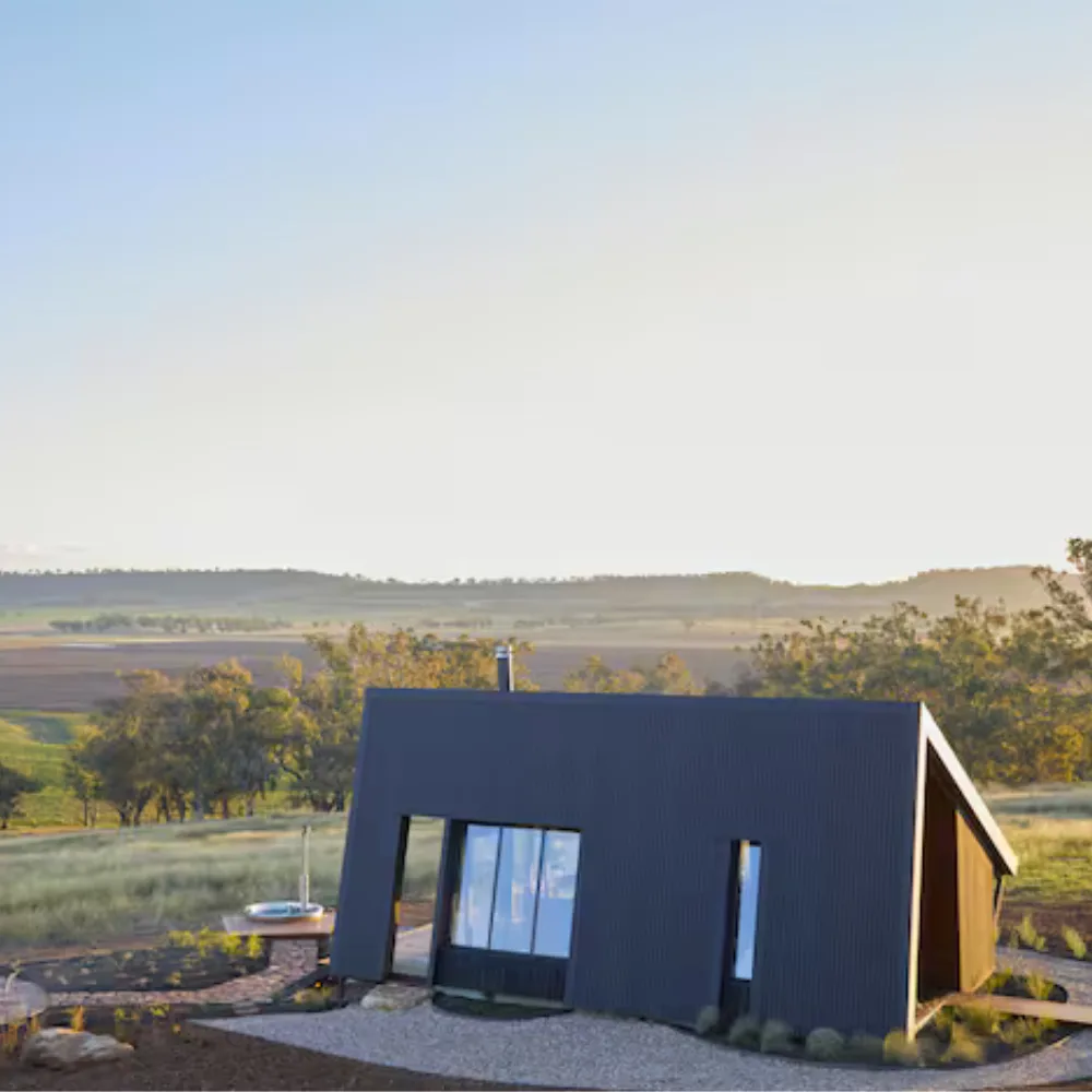 gilay estate on airbnb lifestyle shot of outside of house. house is triangular shaped in black with rectangular windows and an aussie bushland background
