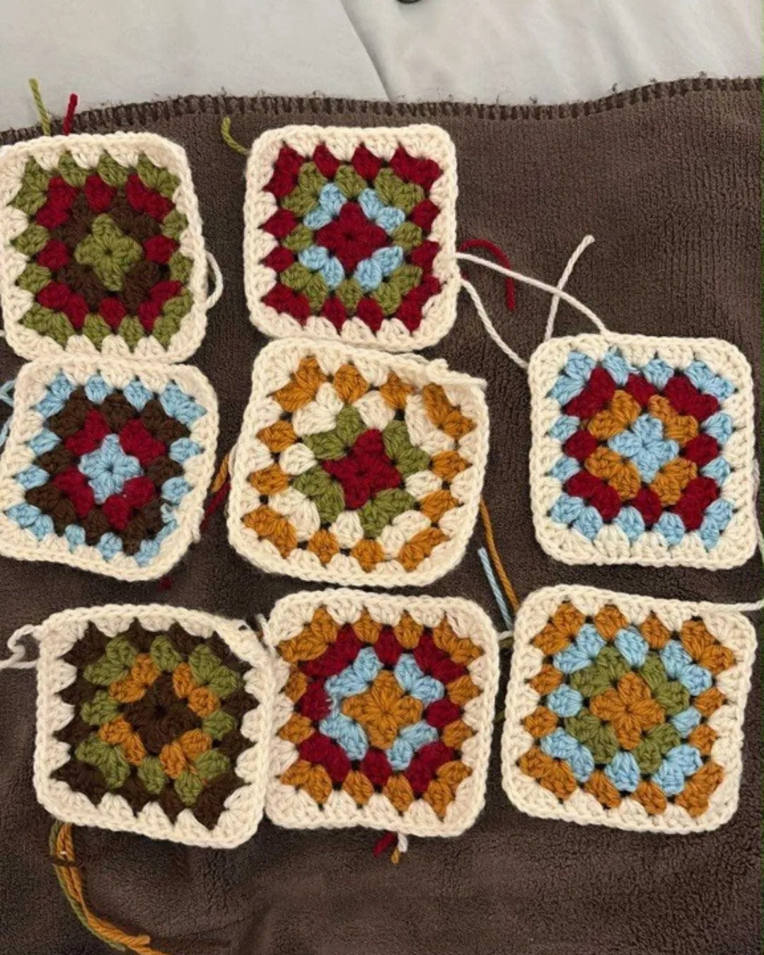 A series of crocheted granny squares in cream, blue, green, brown, and red