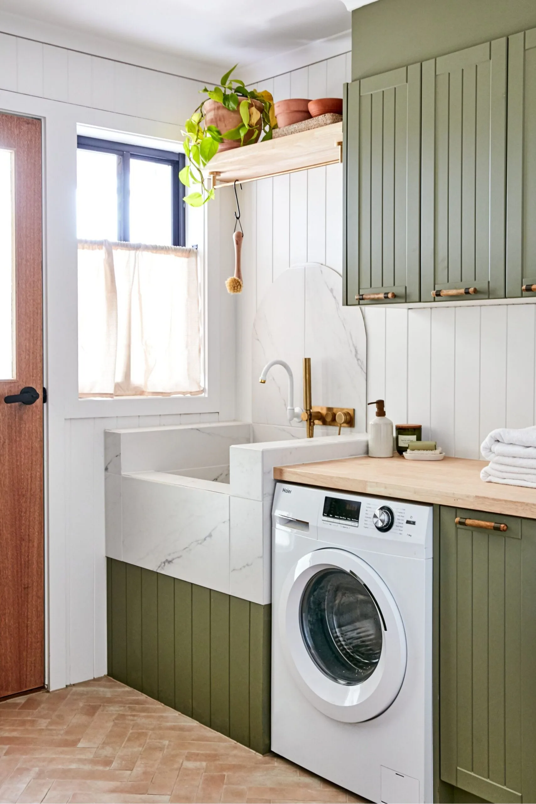 Green panelled laundry doors with in built washing machine and dog-friendly laundry sink in marble