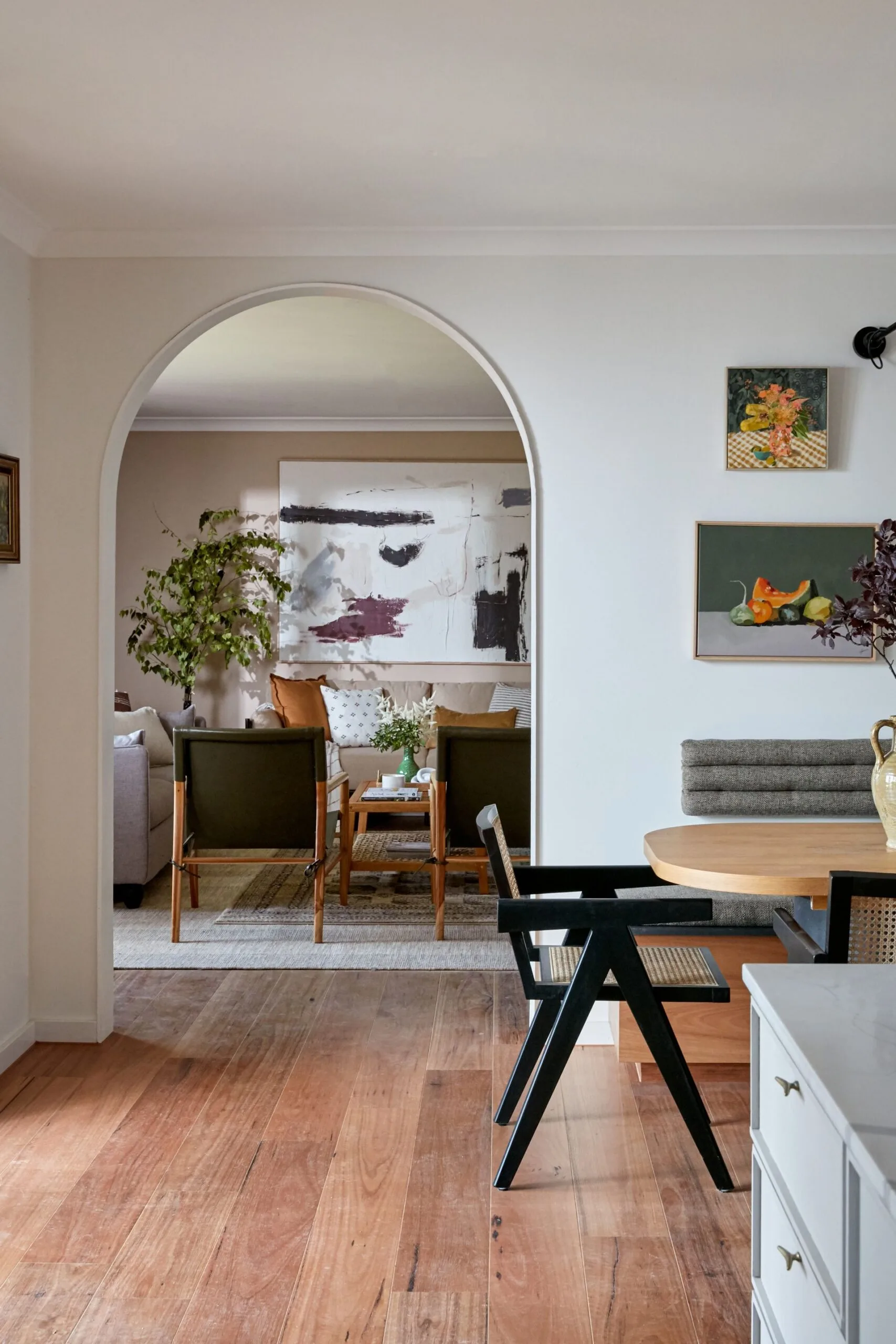 Arched doorway between living room with green sitting chairs and kitchen with rattan black chair and rounded oval table