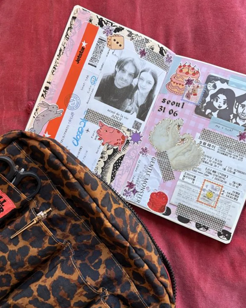 A double-page junk journal spread with a collage oh photos, drawings, receipts, and a plane ticket, against a red background. In the foreground, a cheetah print journal bag sits.