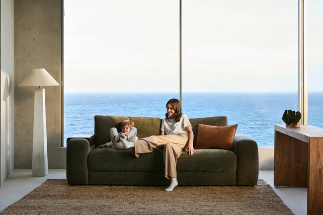 sofa bed in brown with lady sitting on it and ocean views behind