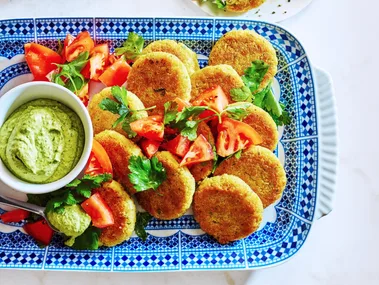 quinoa falafel on tray with green hommus in small dipping bowl and tomato and parsley on top