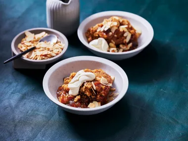 sticky date pudding in two white bowls with extra on the side