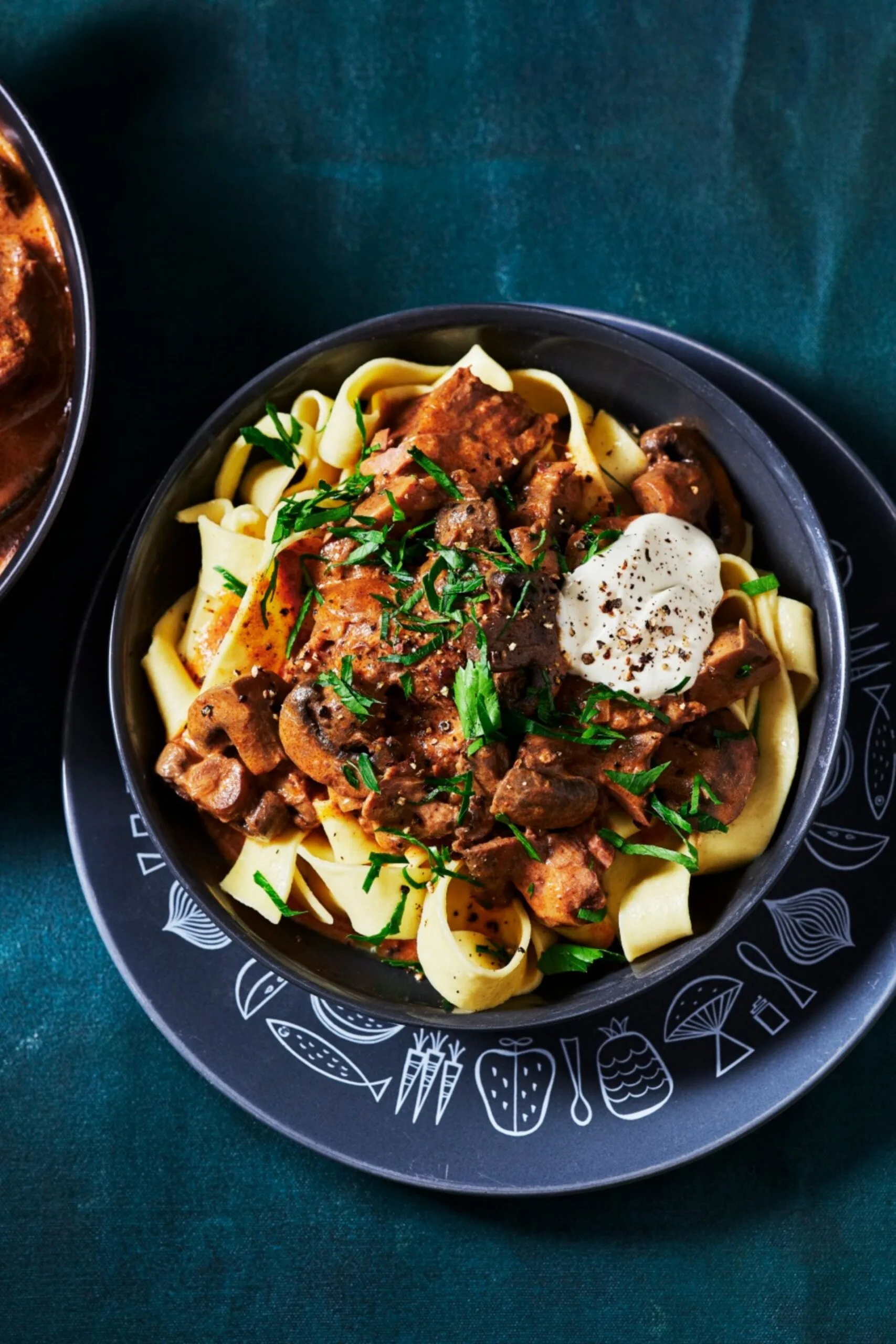 stroganoff pasta in grey bowl with herbs, pepper and a blob of sour cream on top