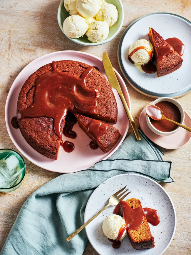 clarissa's sweet potato cake with syrupy glaze on top and piece cut out of it. a plate on the side has a scoop of icecream with piece of cake