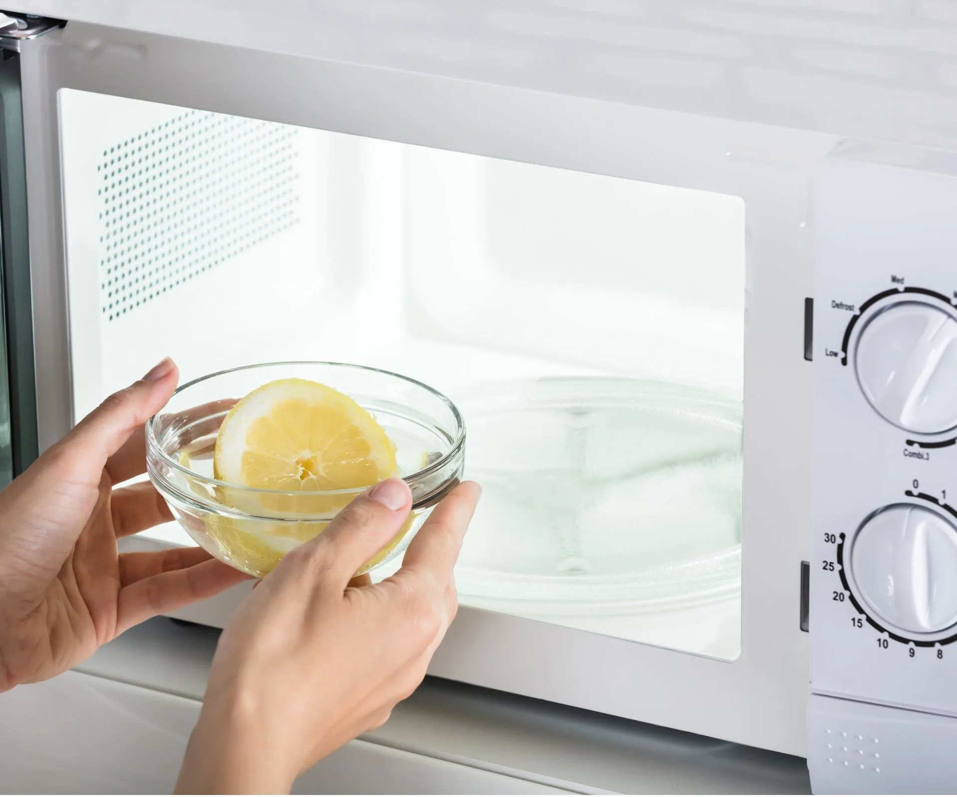 hands putting lemon in glass bowl in microwave