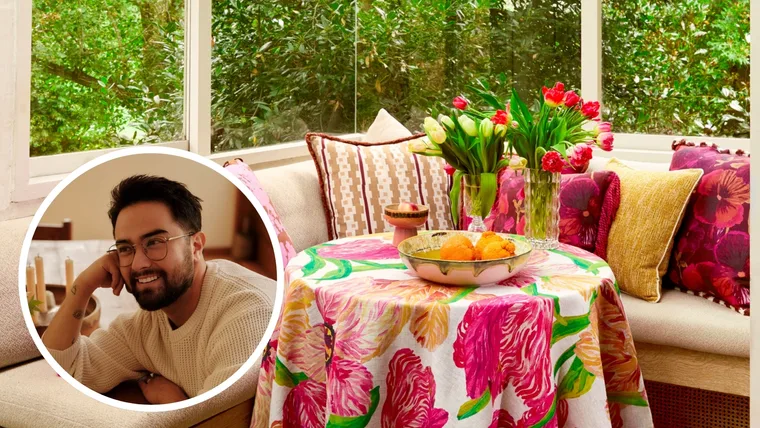 Glass sunroom with banquette seating, pink cushions, a vase of tulips and a floral tablecloth with an image of Jono Fleming