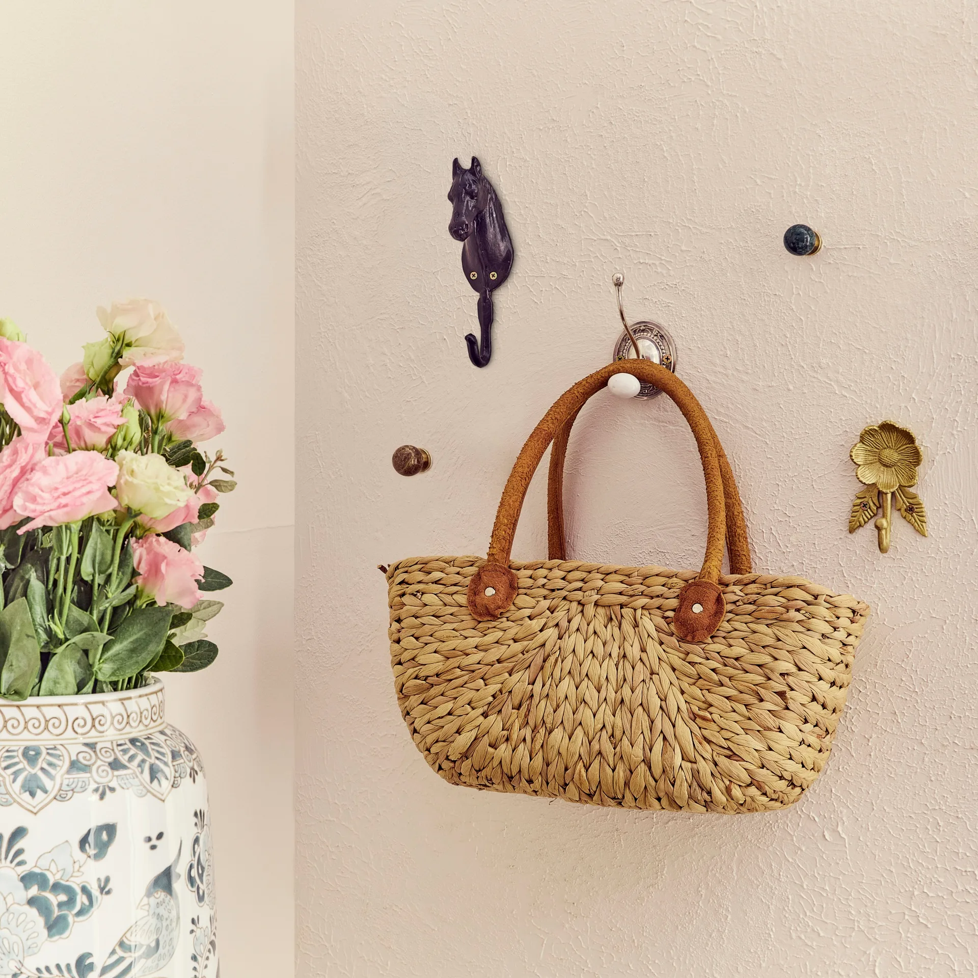 Decorative hooks on a textured rendered beige wall with a cane tote bag