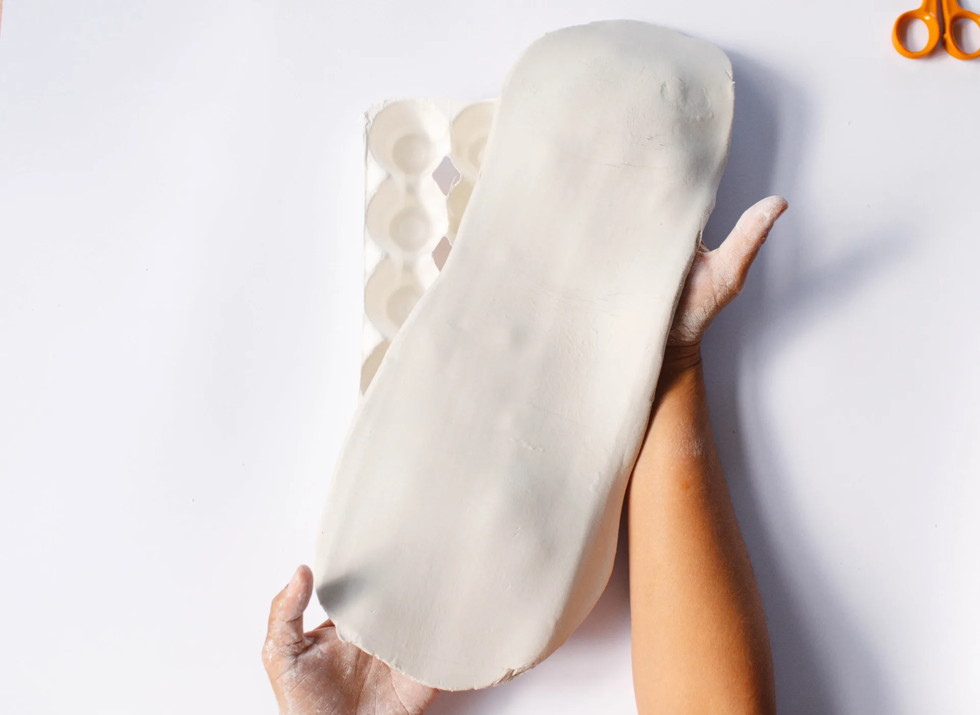 hands stretching clay over egg carton