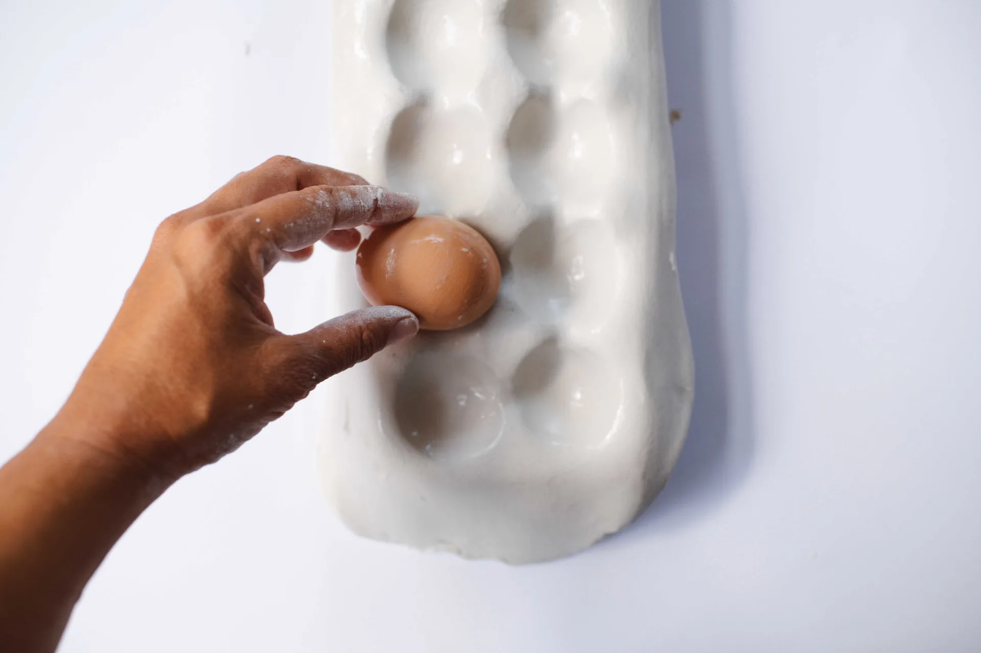 hand placing boiled egg in egg tray to shape clay