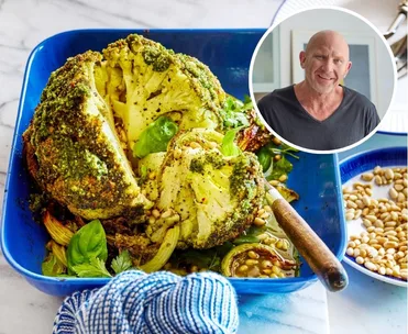 whole baked cauliflower with herby green butter on top, on a blue roasting dish with tea towel on handle. headshot of matt moran in circle in the corner