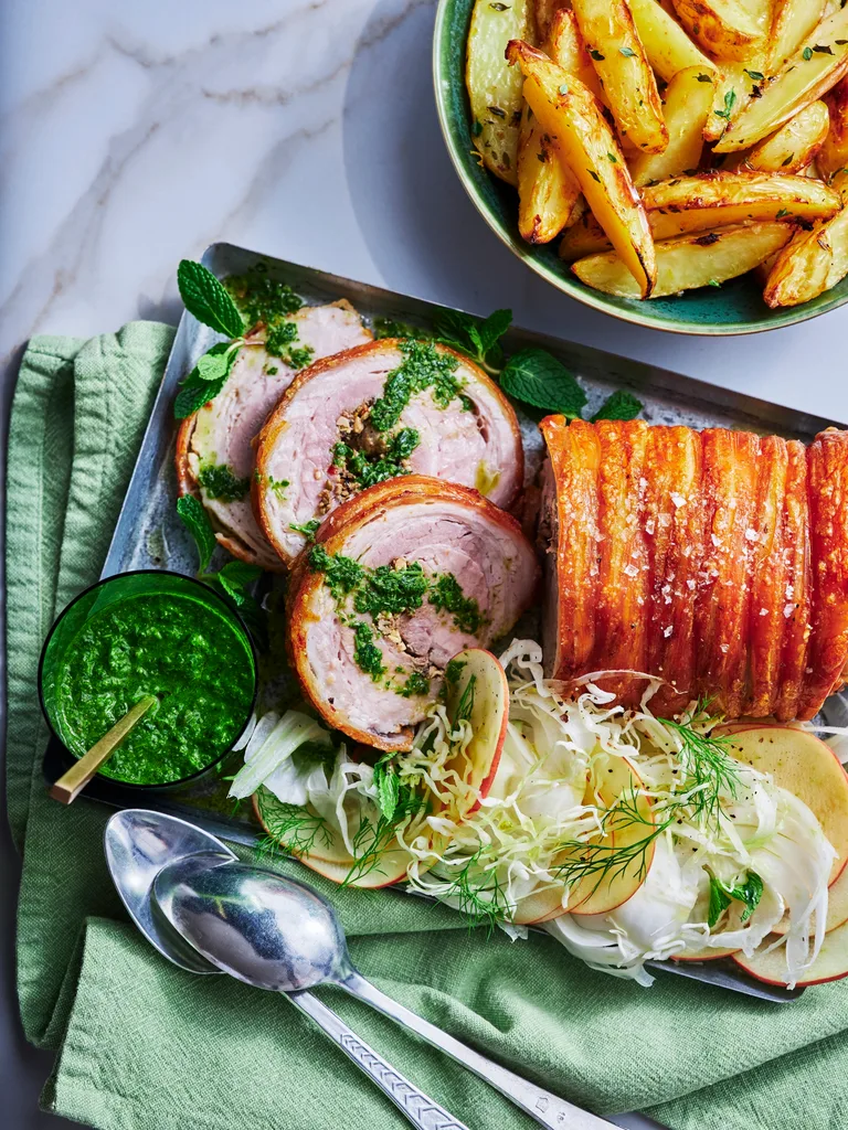 sliced porchetta birds eye view with rolled herbs in the middle and apple fennel slaw placed around it