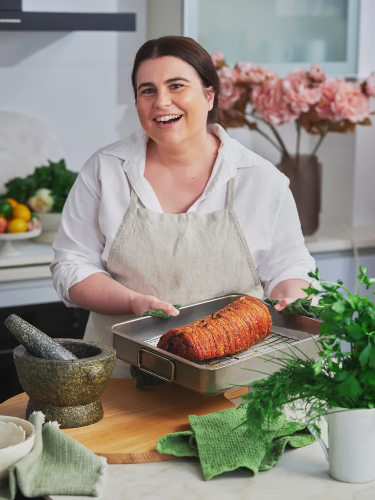 sarah murphy holding tray of porchetta with crispy crackling and bunch of herbs sitting on the side