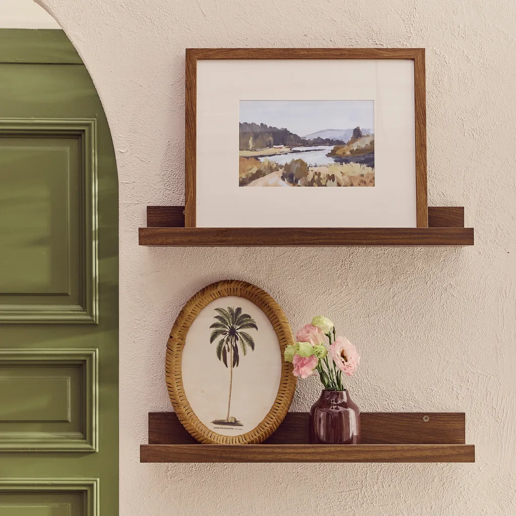 Timber shelves holding framed pictures and a vase on a textured biege wall with green door in the background