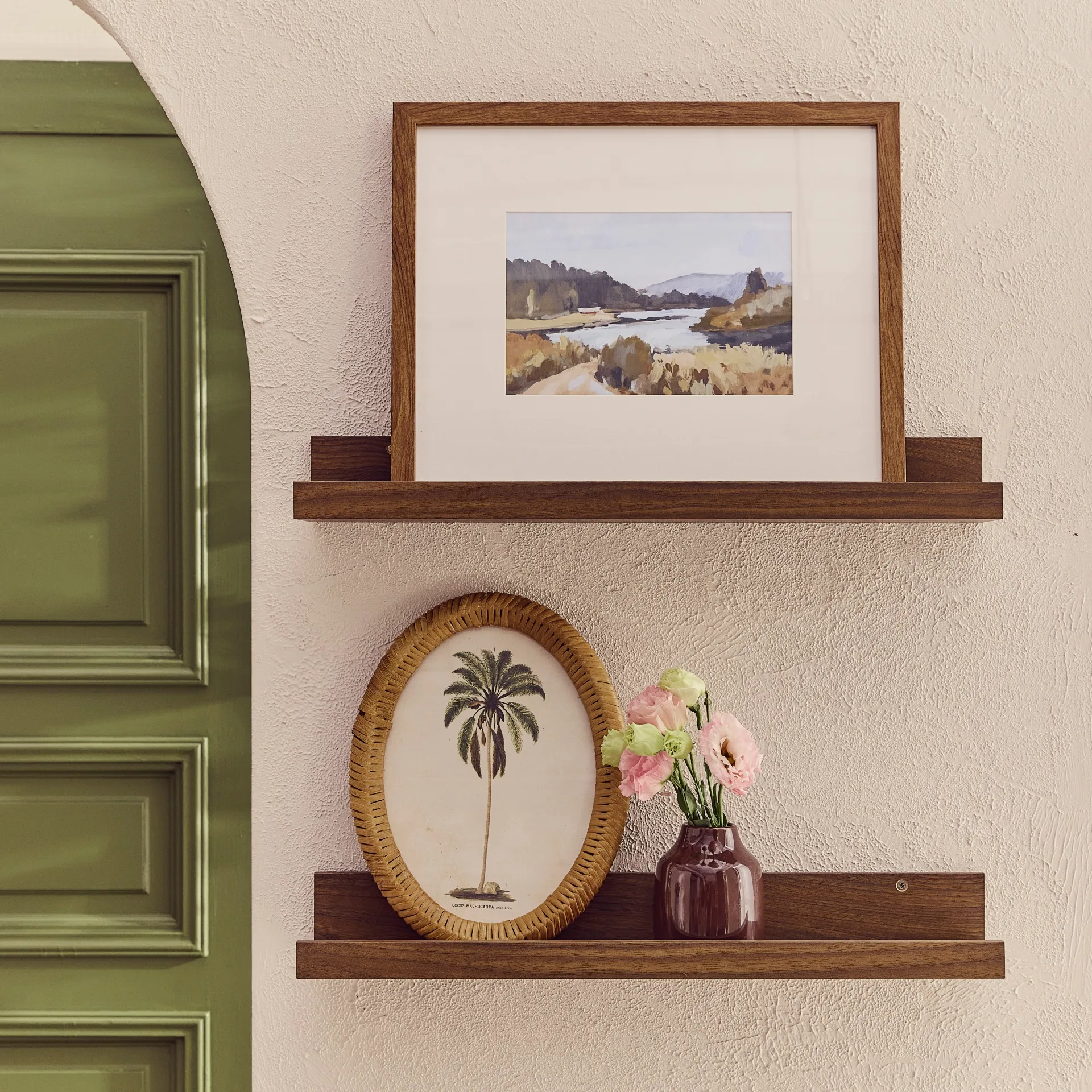 Timber shelves holding framed pictures and a vase on a textured biege wall with green door in the background