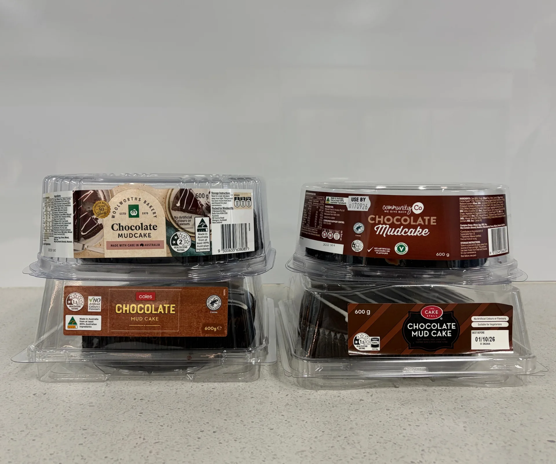 four supermarket mud cakes stacked in pairs with labels showing, from Aldi, IGA, Woolworths and Coles