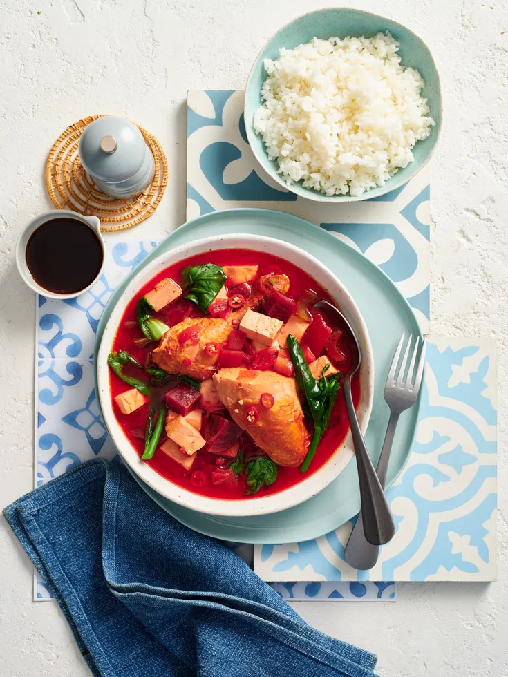 beetroot miso soup with tofu and chicken, colour of soup is warm pink with bowl of rice on the side and patterned blue fabric underneath