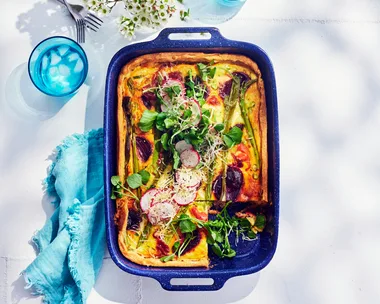 quiche with beetroot asparagus prosciutto and decorated with watercress. In a blue metal tray with sky blue napkin next to it