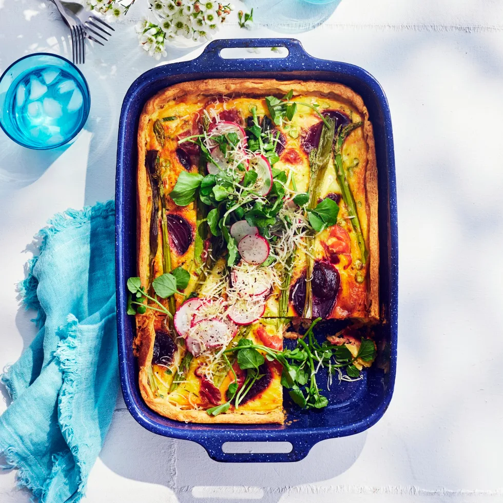 quiche with beetroot asparagus prosciutto and decorated with watercress. In a blue metal tray with sky blue napkin next to it