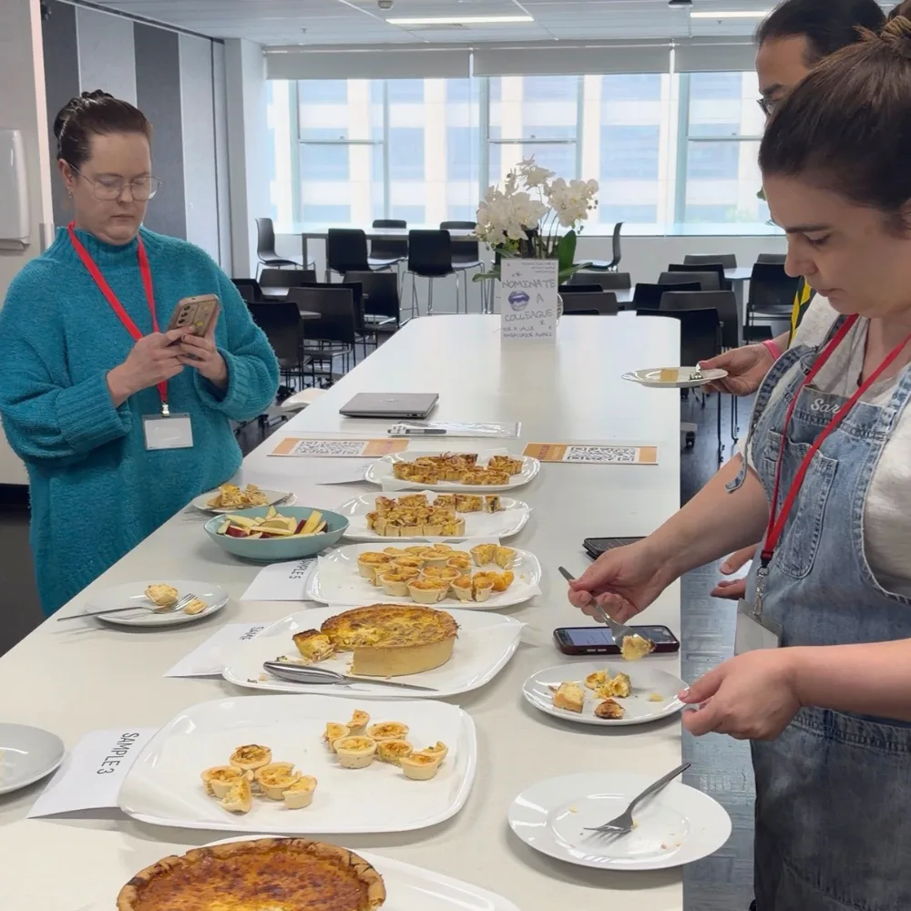 sarah and two other panellists tasting the quiches that are laid out on white trays on a kitchen bench