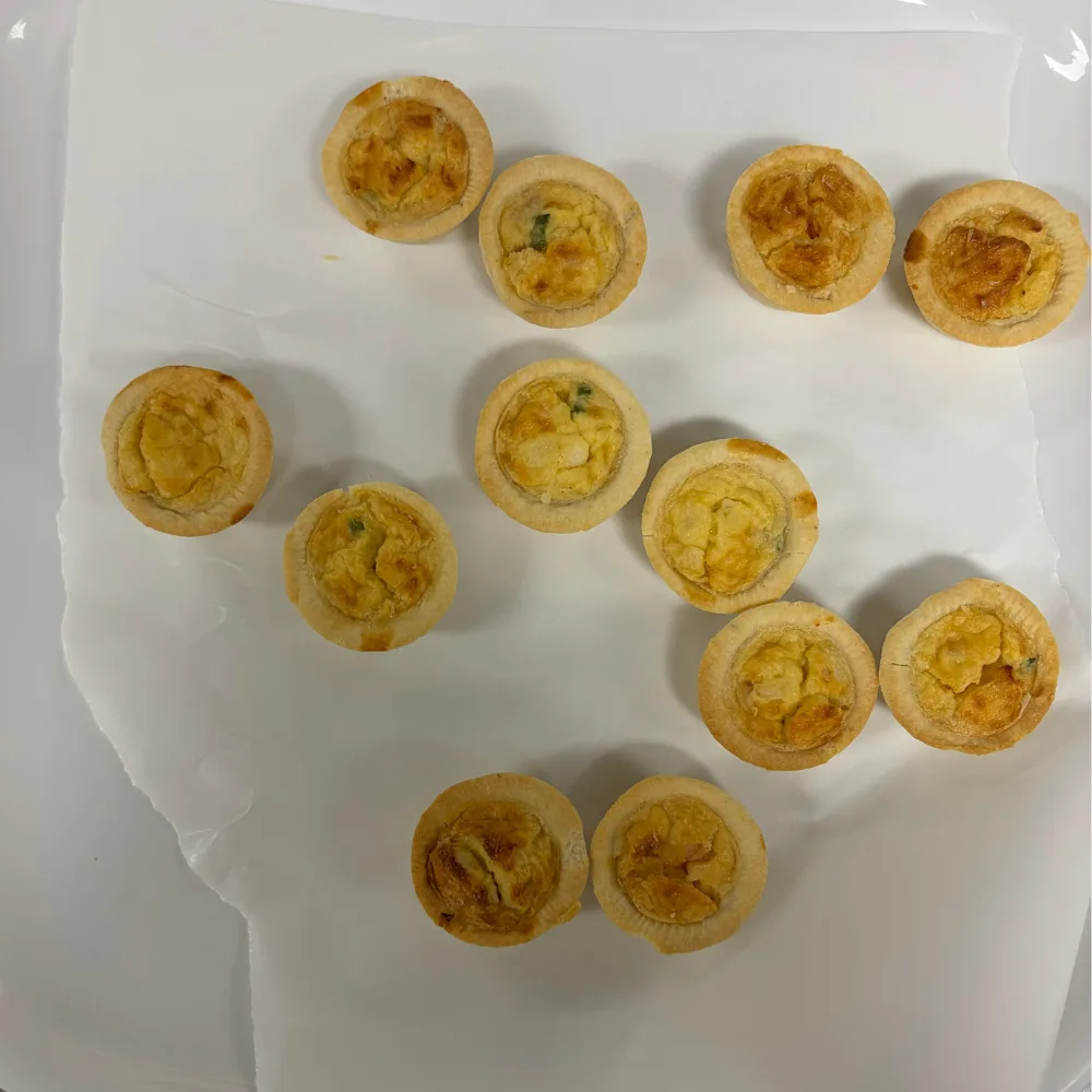 temptation frozen petite quiche lorraines spread out over white tray, tops of them pale