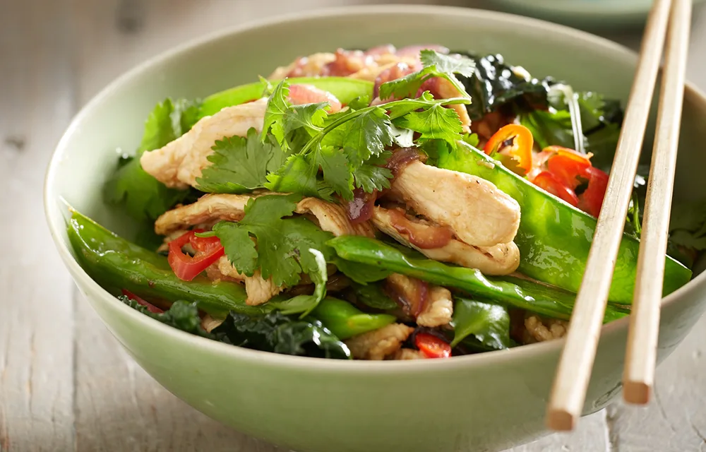 Spicy chicken stir fry in a bowl with snow peas and chopsticks