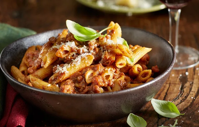 eggplant ragu with leaf of basil on top in black bowl