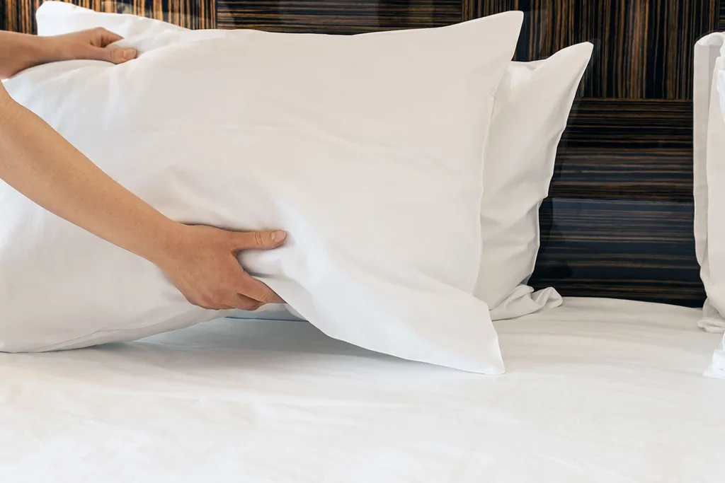 Woman placing pillows on bed.