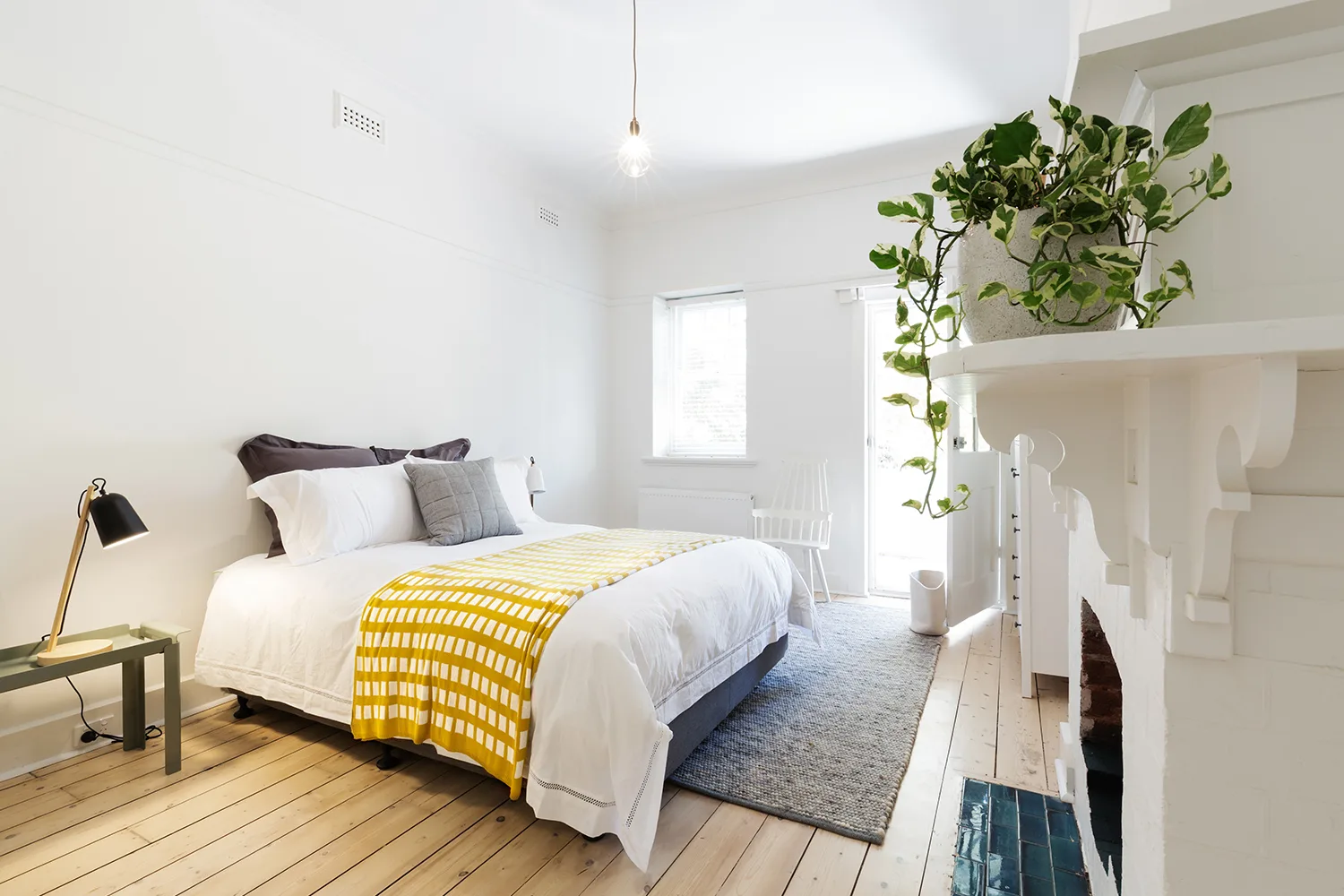 bedroom with timber floors, white walls, bedding and fireplace