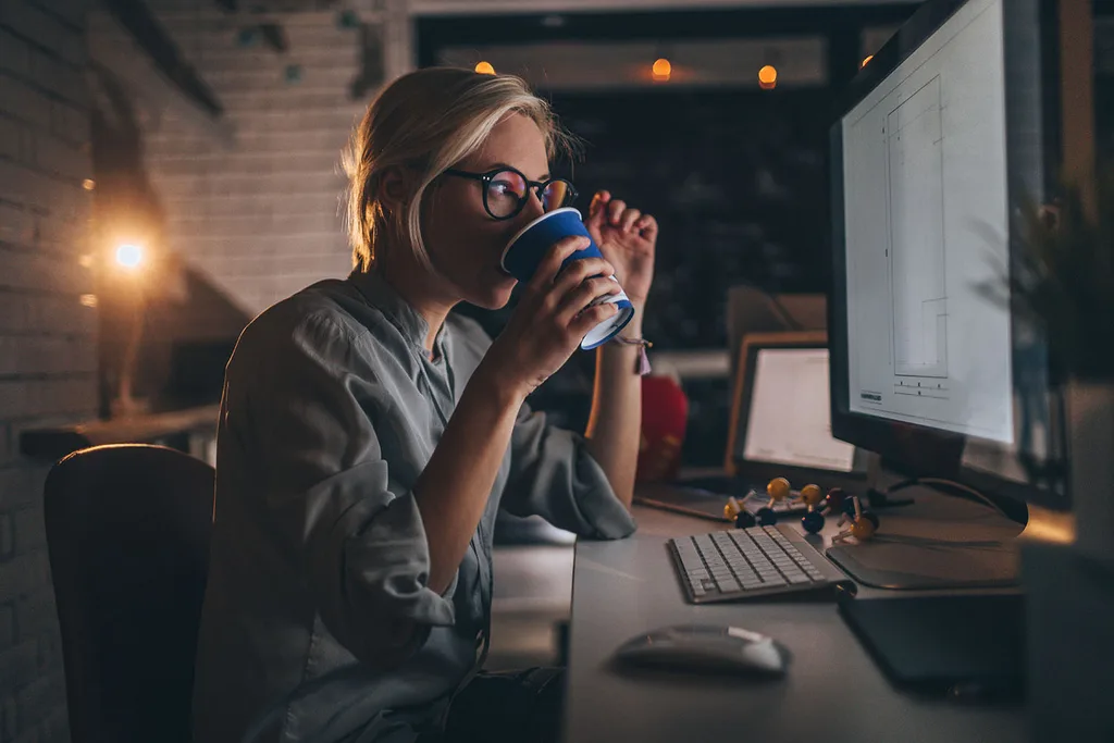 woman drinking coffee looking at computer screen in dark