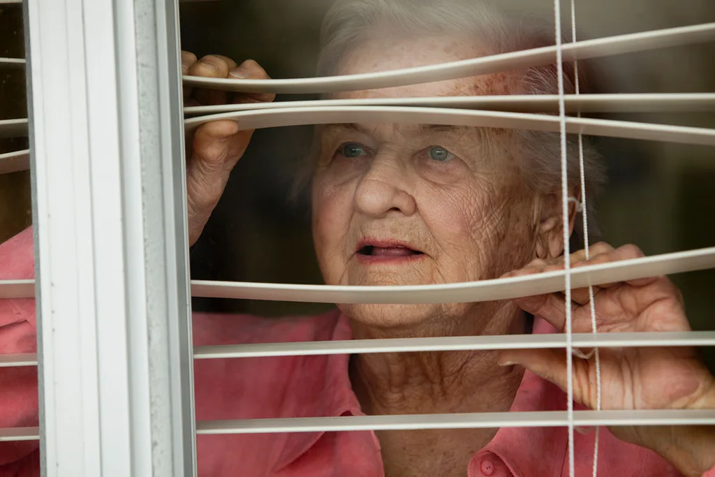 woman looking through window blinds