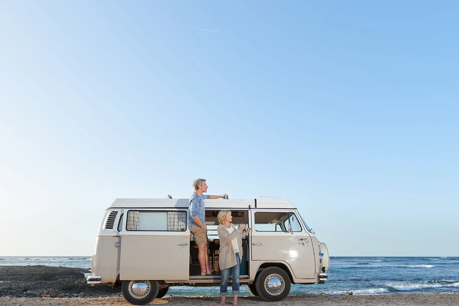 man and woman standing in from of kombi on coast