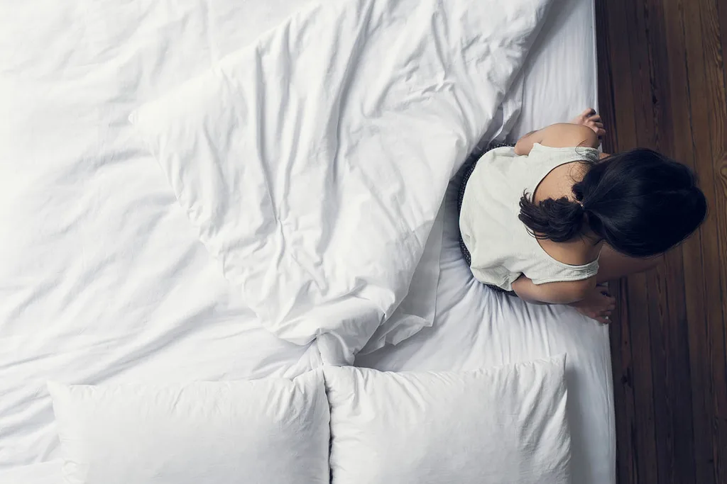 woman sitting on edge of white bed