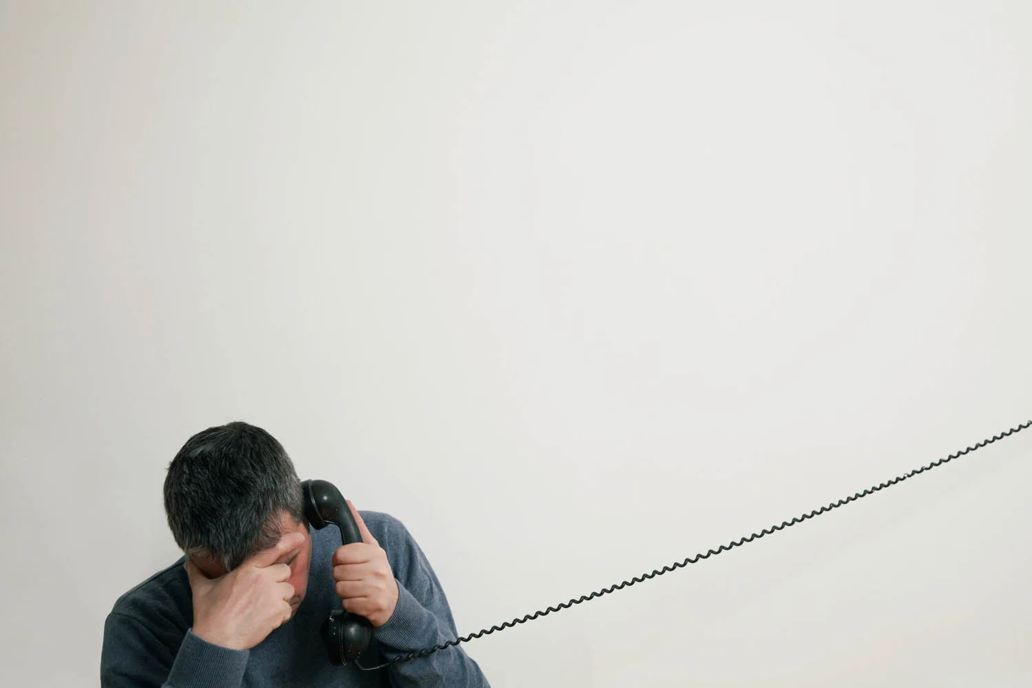 man covering face and talking on landline phone