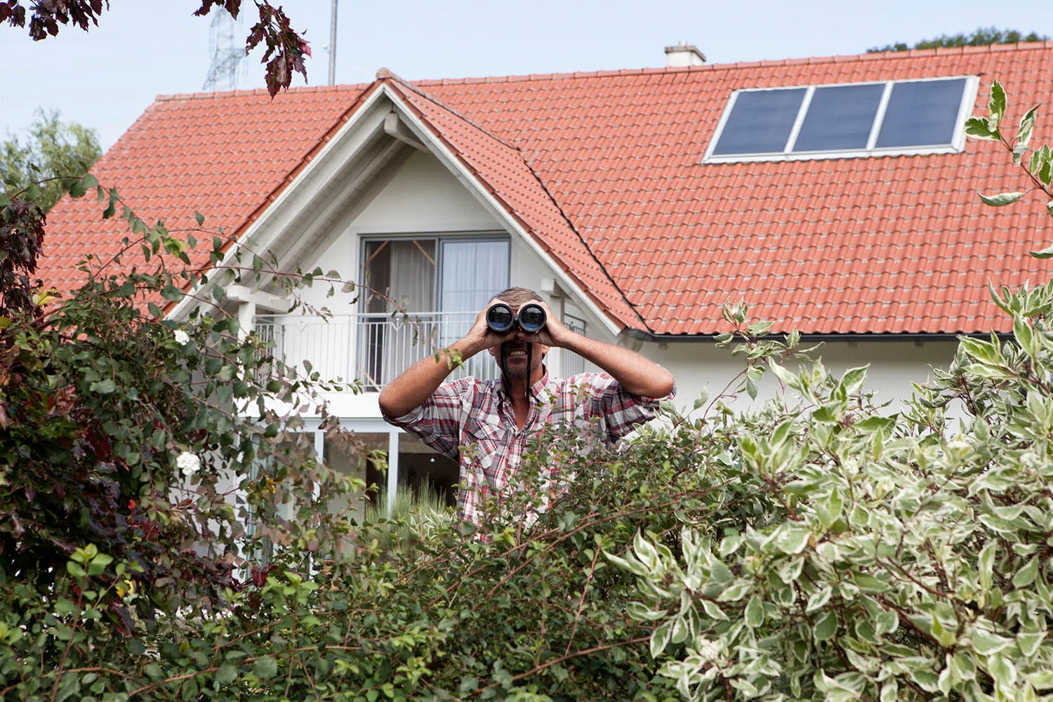 man looking over bush with binoculars