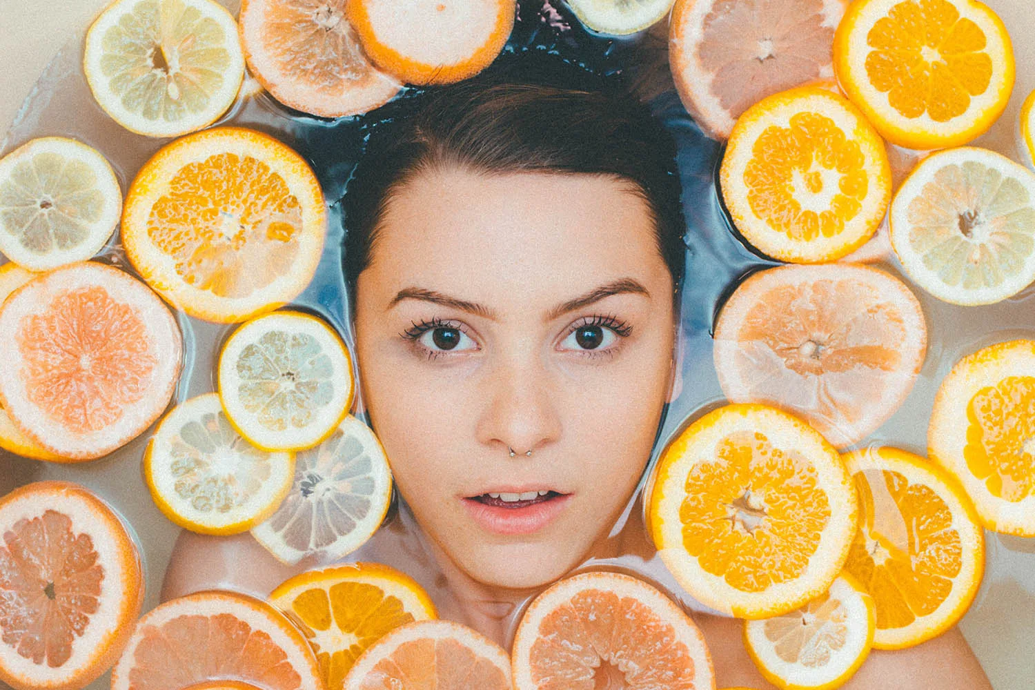 woman face in bath of oranges