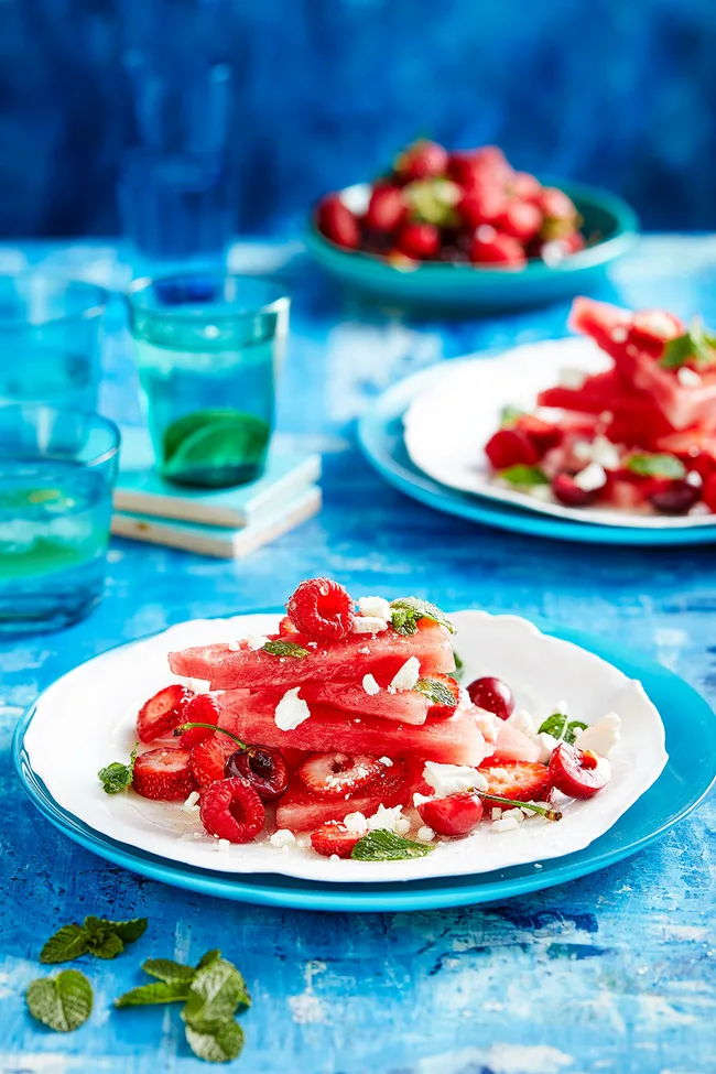 Red fruit salad featuring watermelon and mixed berries topped with sugar syrup