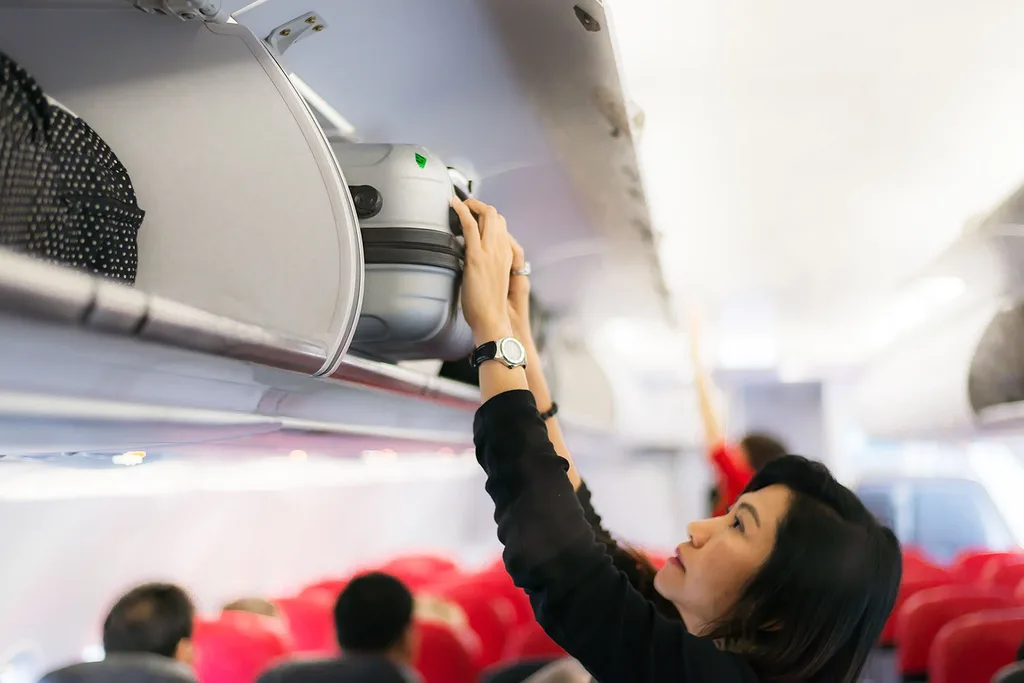 woman putting suitcase into over head locker