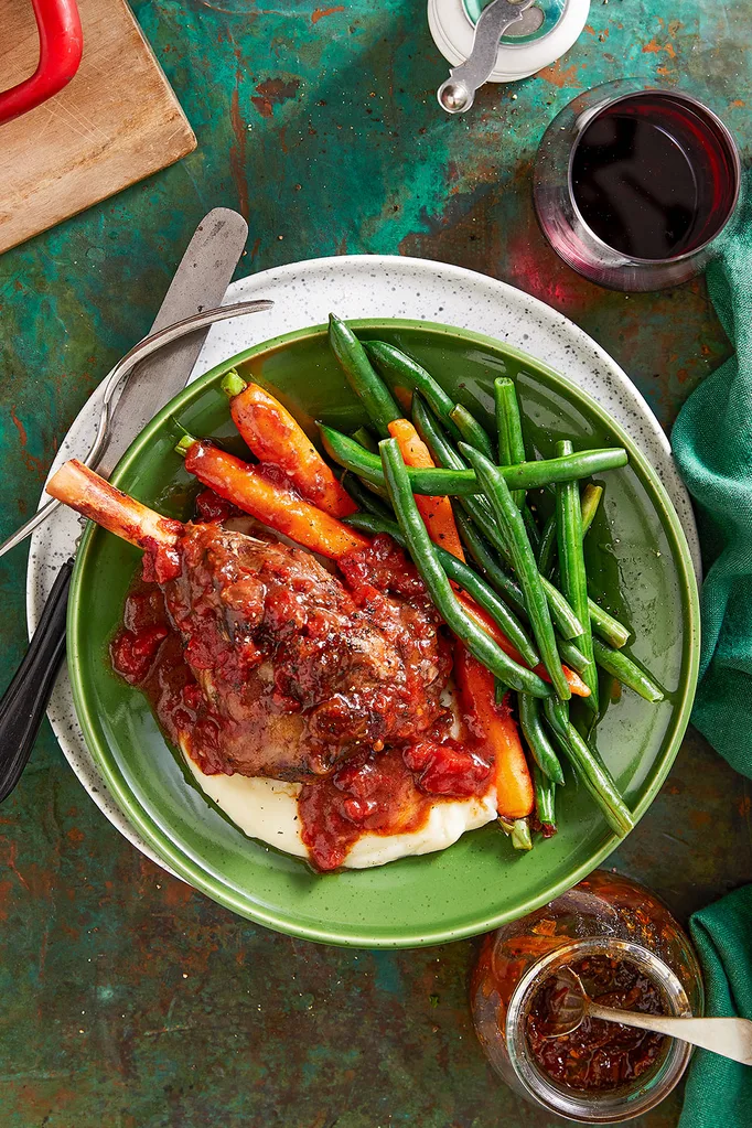 Slow cooker lamb shanks in red wine sauce plated up next to steamed beans and carrots