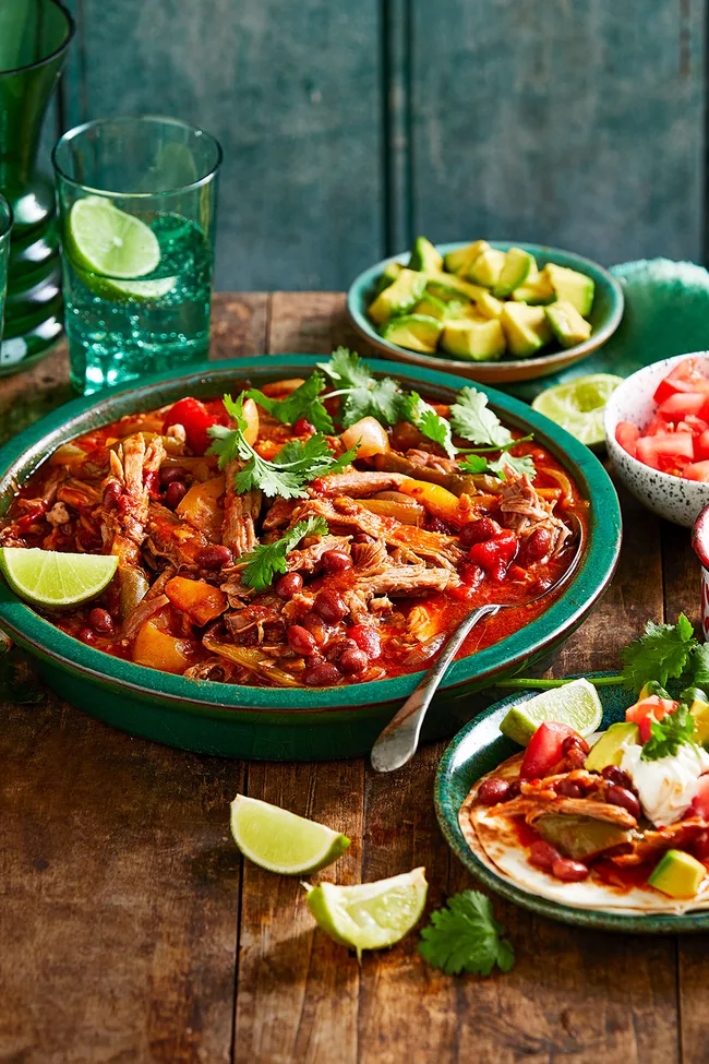 mexican pork with beans in large green bowl with slices of lime