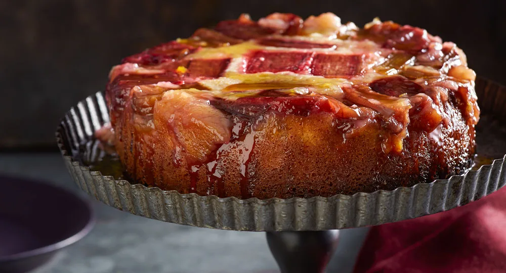 rhubarb upside down cake with slices of rhubarb on top of cake on black pie stand