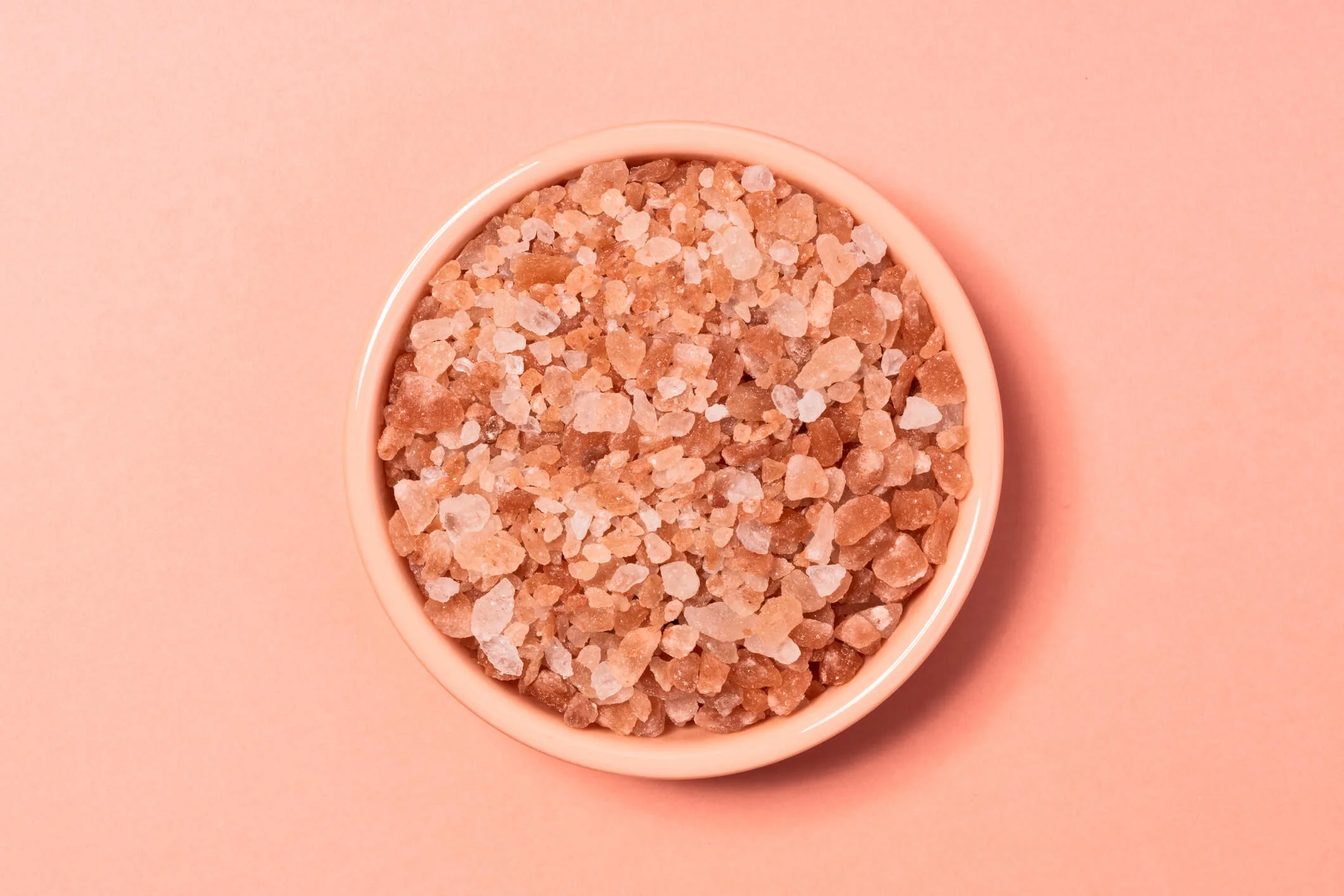 A bowl of pink Himalayan rock salt on a pink background