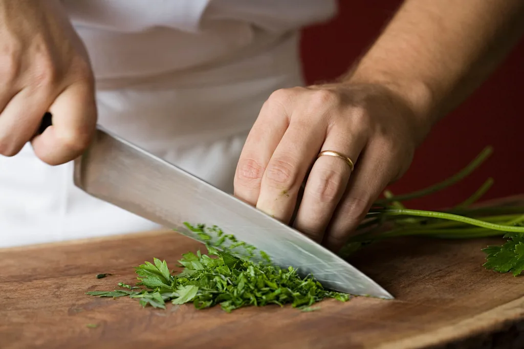 A chef cutting herbs on a wooden chopping board