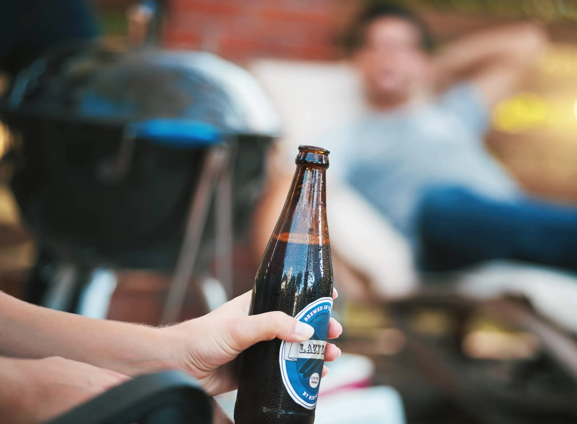 Man holding beer while sitting outside with friends next to a bbq