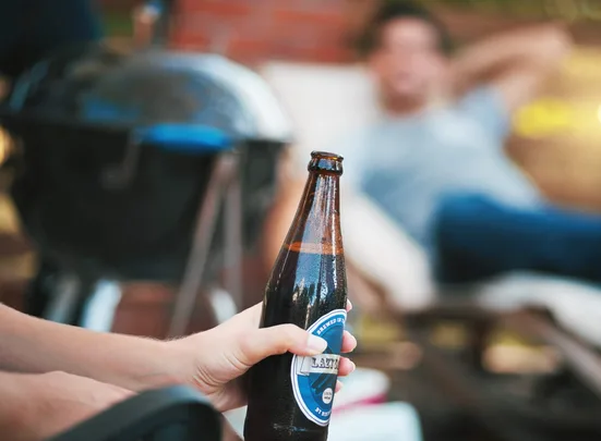 Man holding beer while sitting outside with friends next to a bbq