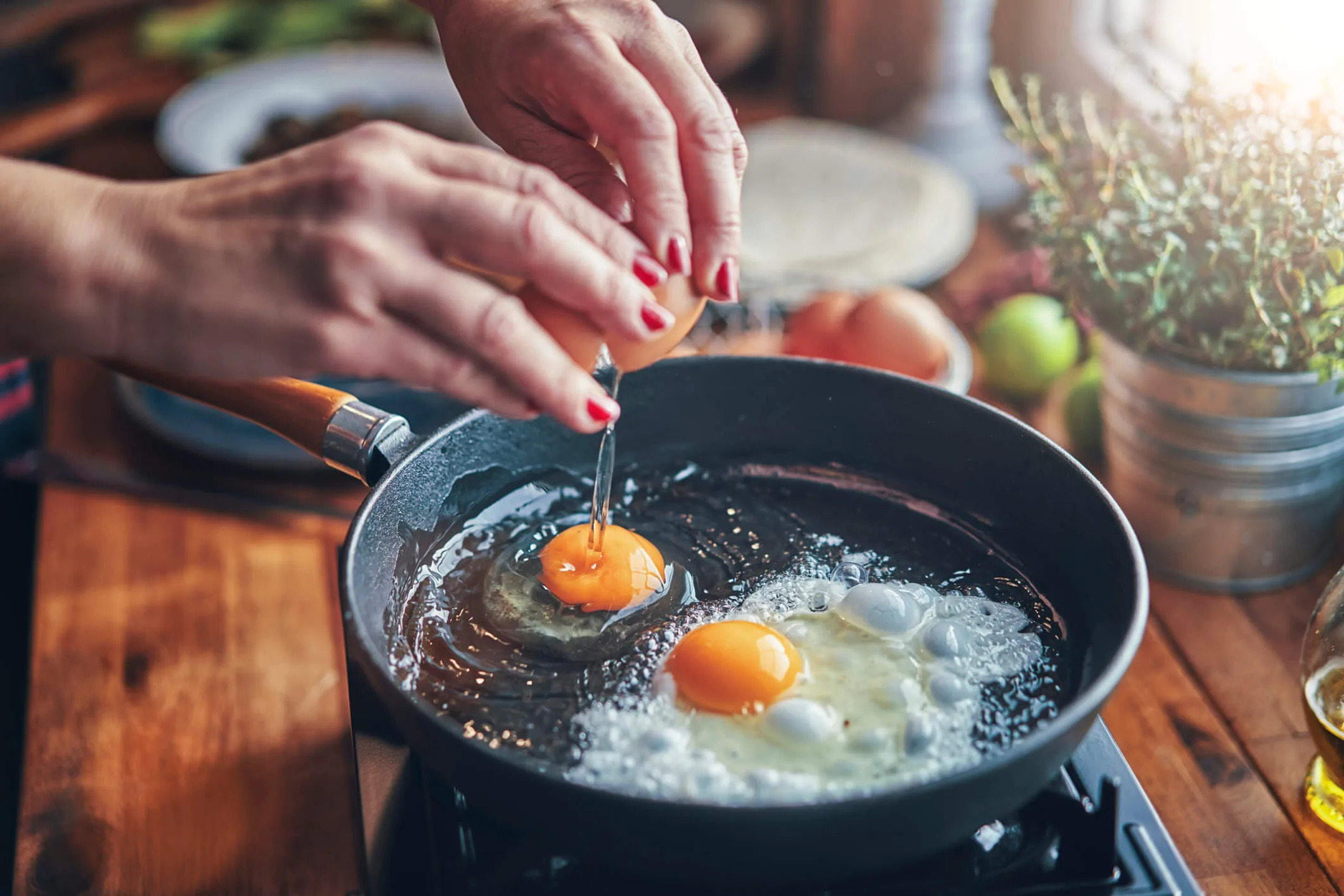 Cracking eggs into a frypan with a sunflare in the top right of the photo