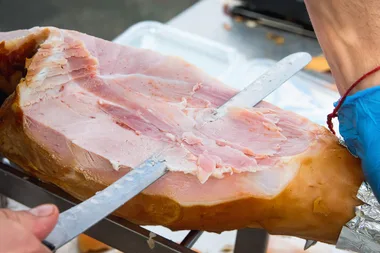 A man cutting a leg of ham with a long knife