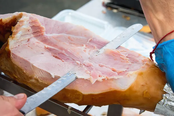 A man cutting a leg of ham with a long knife
